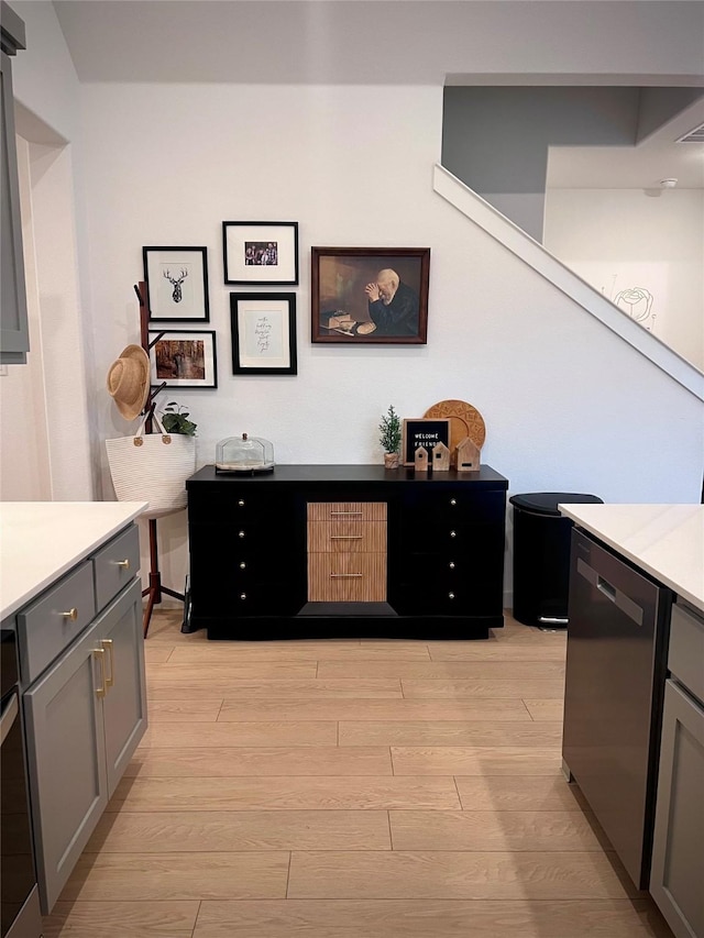 kitchen with stainless steel dishwasher, gray cabinets, and light wood-type flooring