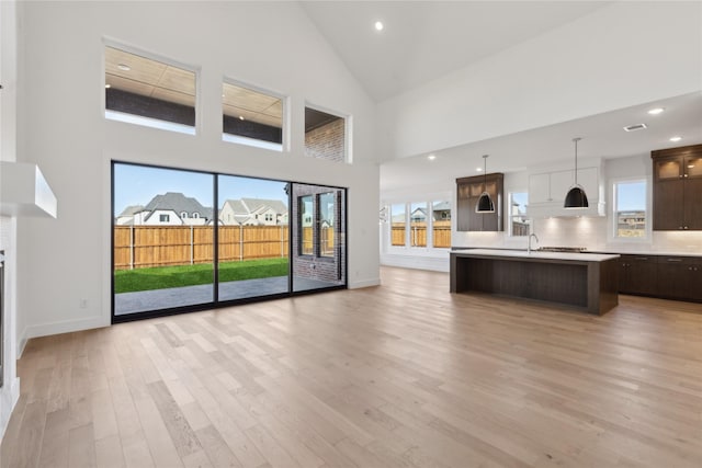 kitchen featuring light countertops, light wood-style flooring, open floor plan, dark brown cabinetry, and an island with sink