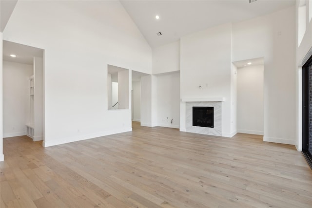 unfurnished living room featuring high vaulted ceiling, light wood-type flooring, a fireplace, and baseboards