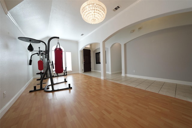 exercise room featuring crown molding, vaulted ceiling, an inviting chandelier, and light hardwood / wood-style flooring