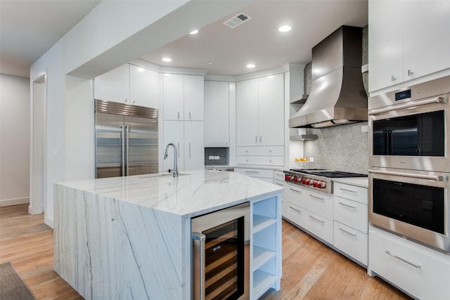 kitchen featuring wine cooler, wall chimney range hood, a center island with sink, sink, and stainless steel appliances