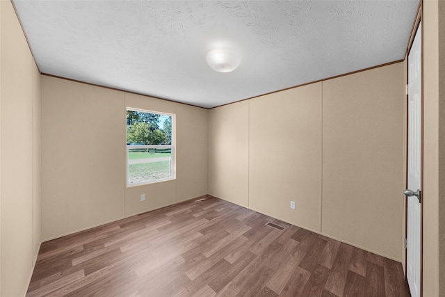 empty room with a textured ceiling and light hardwood / wood-style flooring