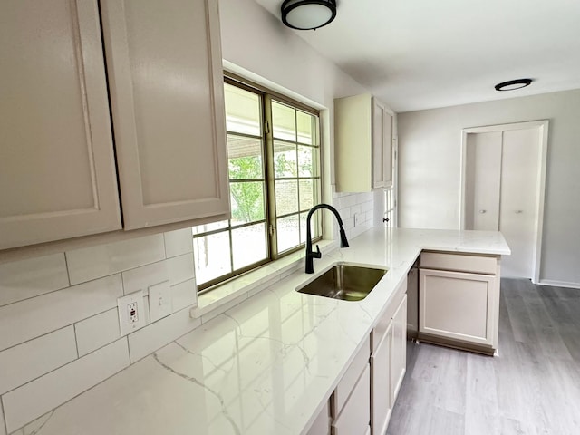 kitchen featuring kitchen peninsula, decorative backsplash, light stone countertops, and sink