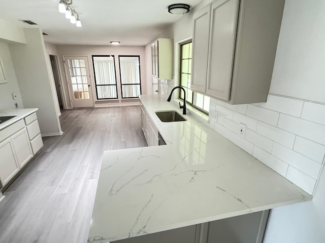 kitchen featuring light stone countertops, decorative backsplash, kitchen peninsula, and sink