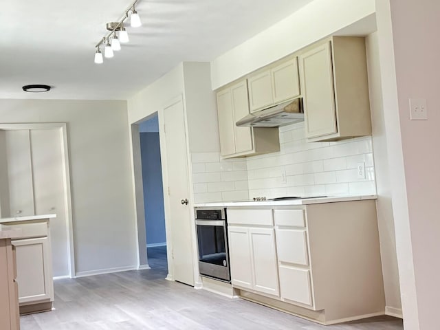 kitchen with decorative backsplash, stainless steel oven, light wood-type flooring, cooktop, and cream cabinets