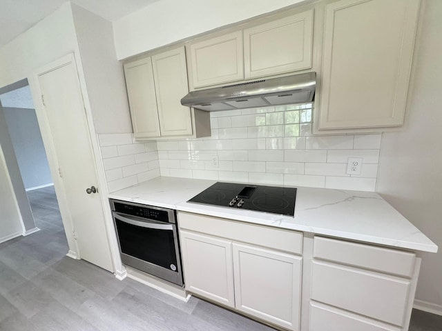 kitchen featuring decorative backsplash, stainless steel oven, black electric cooktop, light stone countertops, and light hardwood / wood-style flooring