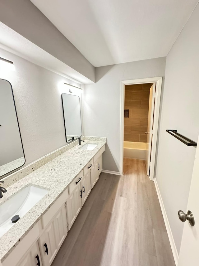 bathroom with hardwood / wood-style flooring, tiled shower / bath combo, and vanity