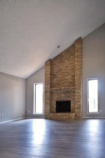 unfurnished living room featuring lofted ceiling, a healthy amount of sunlight, a brick fireplace, and dark hardwood / wood-style floors