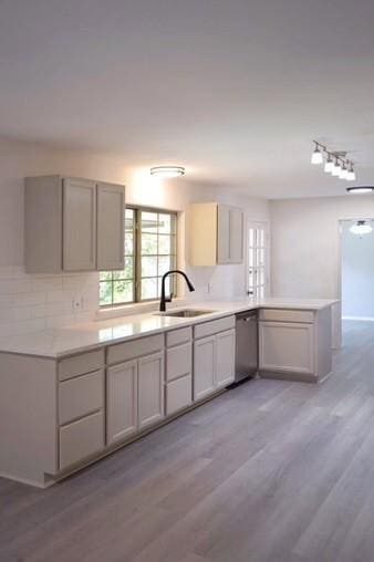 kitchen featuring light hardwood / wood-style floors, stainless steel dishwasher, kitchen peninsula, and sink