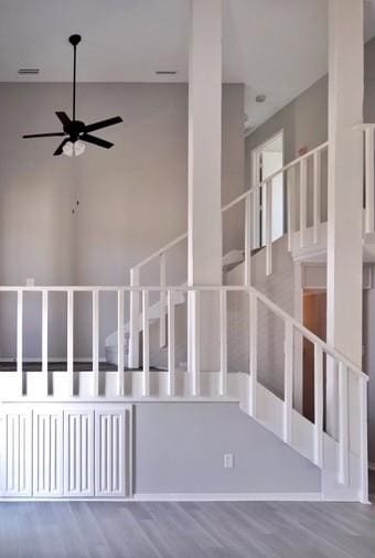 stairway with ceiling fan, a towering ceiling, and wood-type flooring