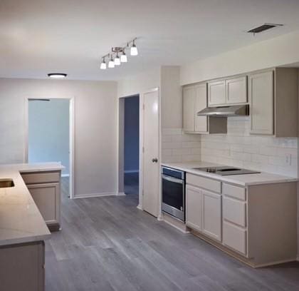 kitchen featuring stainless steel oven, decorative backsplash, gray cabinetry, and hardwood / wood-style floors