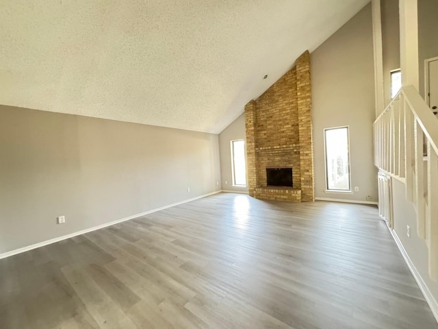 unfurnished living room with a textured ceiling, a fireplace, hardwood / wood-style floors, and high vaulted ceiling