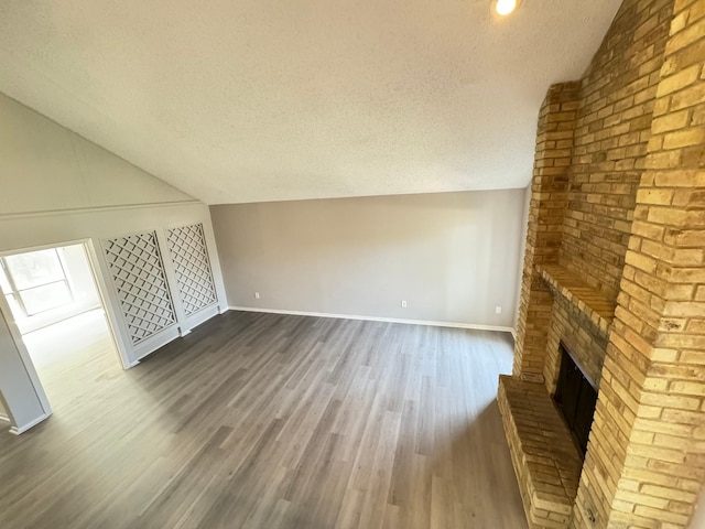 unfurnished living room with a brick fireplace, a textured ceiling, dark hardwood / wood-style floors, and lofted ceiling