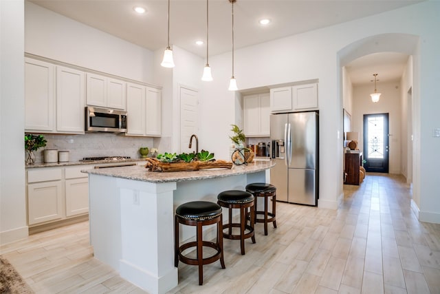 kitchen featuring white cabinetry, appliances with stainless steel finishes, a center island with sink, and hanging light fixtures