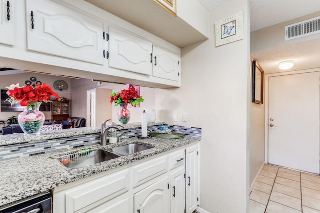 kitchen with white cabinets, sink, light stone counters, light tile patterned floors, and stainless steel dishwasher