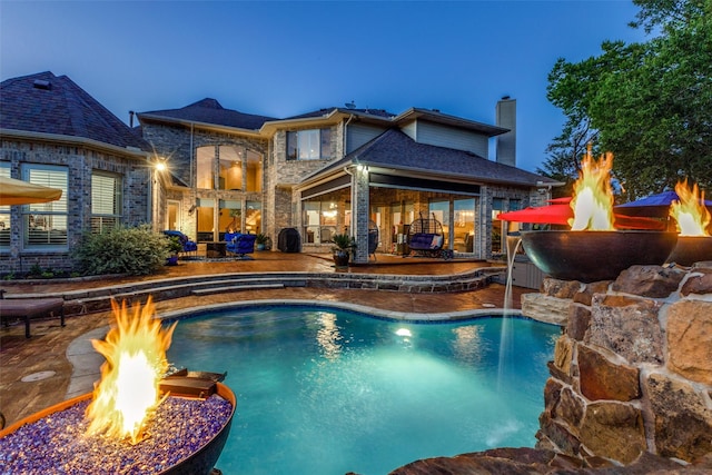 pool at dusk with an outdoor fire pit and a patio