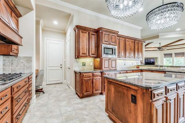 kitchen featuring ceiling fan with notable chandelier, appliances with stainless steel finishes, a kitchen island, sink, and hanging light fixtures