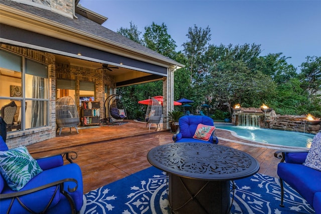 patio terrace at dusk featuring ceiling fan, a swimming pool side deck, an outdoor hangout area, and pool water feature