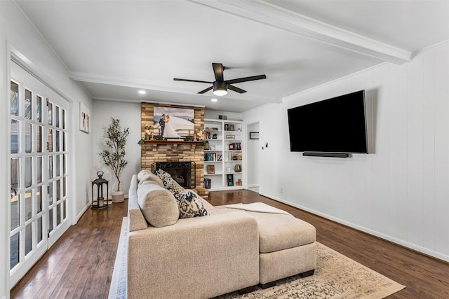 living room with built in shelves, beamed ceiling, dark hardwood / wood-style floors, and a stone fireplace