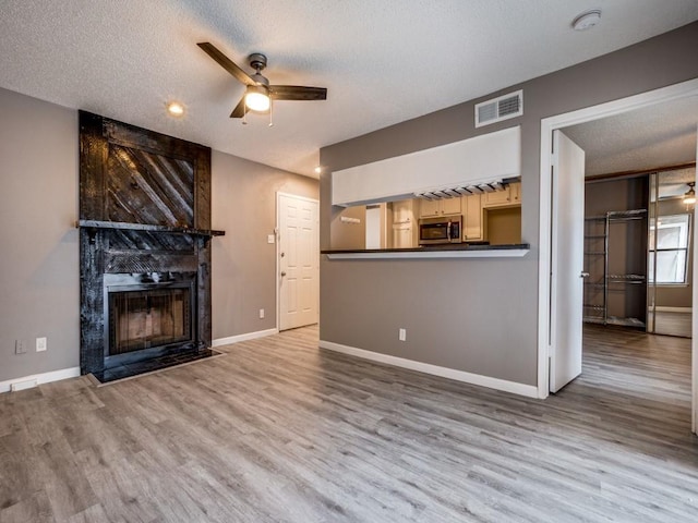 unfurnished living room with hardwood / wood-style flooring, a large fireplace, a textured ceiling, and ceiling fan