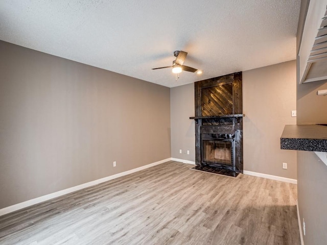 unfurnished living room with wood-type flooring, a textured ceiling, ceiling fan, and a large fireplace