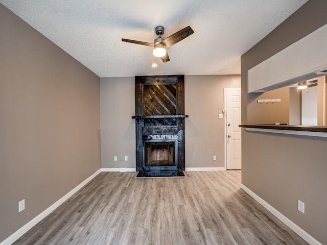 unfurnished living room with a textured ceiling, ceiling fan, hardwood / wood-style floors, and a tile fireplace