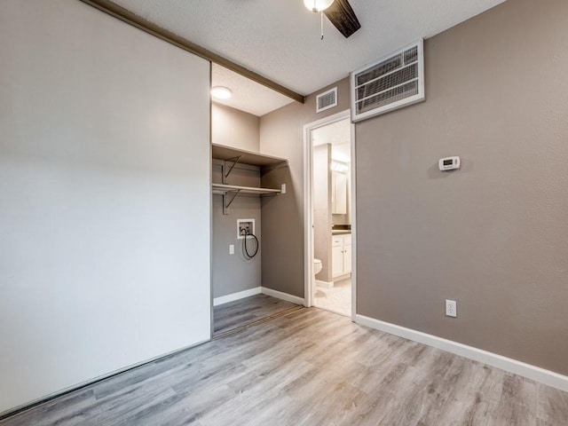 unfurnished bedroom featuring ceiling fan, light hardwood / wood-style floors, a textured ceiling, a walk in closet, and a closet