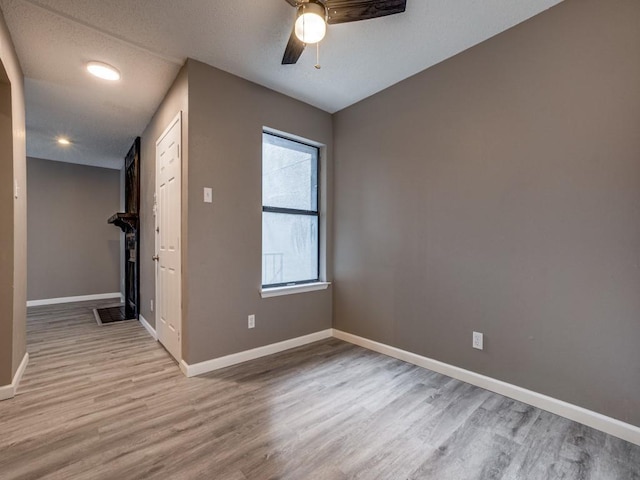 spare room featuring ceiling fan, a textured ceiling, light hardwood / wood-style flooring, and a tiled fireplace