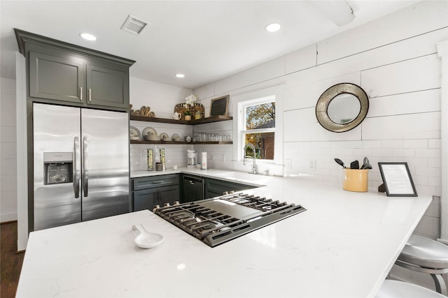 kitchen with kitchen peninsula, stainless steel refrigerator with ice dispenser, gas cooktop, sink, and light stone countertops