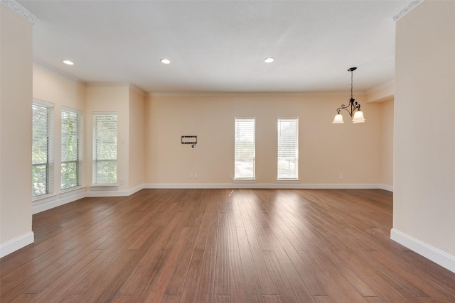 empty room featuring a wealth of natural light, ornamental molding, a chandelier, and hardwood / wood-style flooring