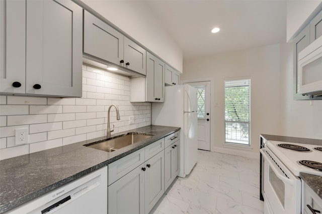 kitchen featuring white appliances, dark stone countertops, sink, backsplash, and gray cabinets