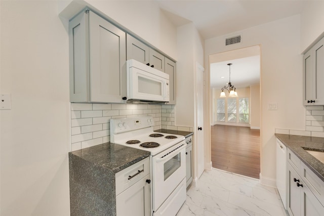 kitchen featuring backsplash, white appliances, a chandelier, and dark stone counters