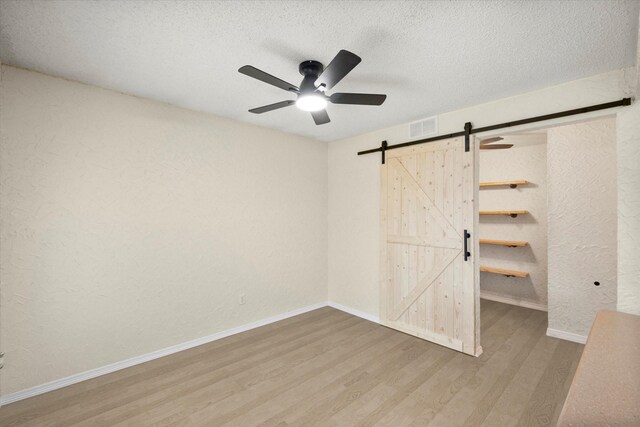 unfurnished bedroom featuring ceiling fan, a barn door, and a textured ceiling