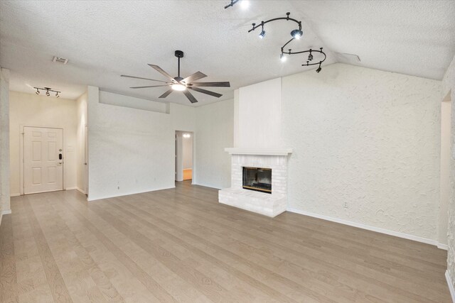 unfurnished living room with ceiling fan, vaulted ceiling, track lighting, and a textured ceiling