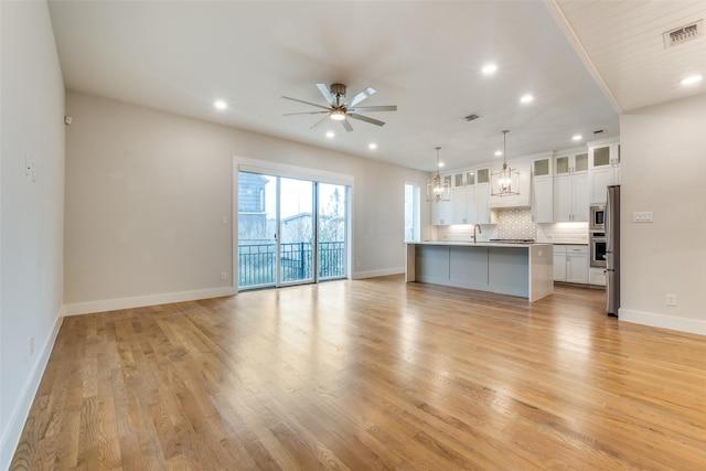 unfurnished living room featuring sink, ceiling fan with notable chandelier, and light hardwood / wood-style flooring