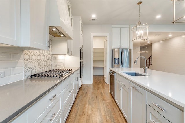 kitchen with premium range hood, appliances with stainless steel finishes, white cabinets, and sink