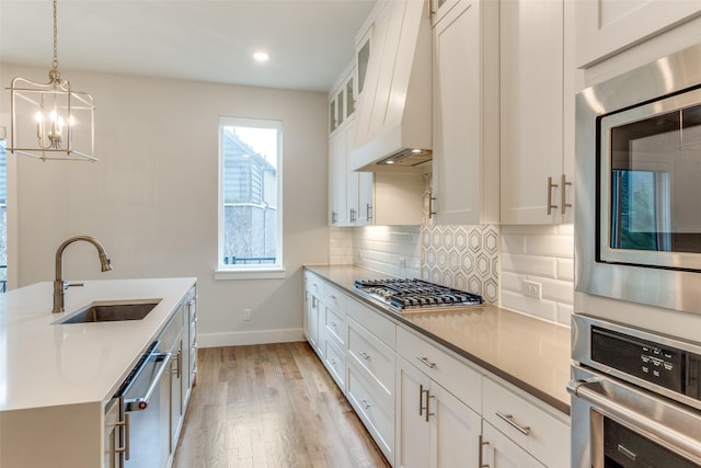 kitchen featuring appliances with stainless steel finishes, white cabinetry, sink, backsplash, and hanging light fixtures