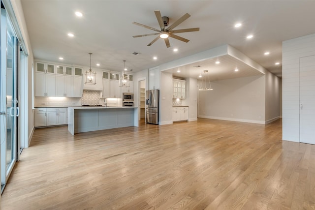 kitchen featuring a spacious island, decorative light fixtures, white cabinetry, stainless steel appliances, and light hardwood / wood-style flooring