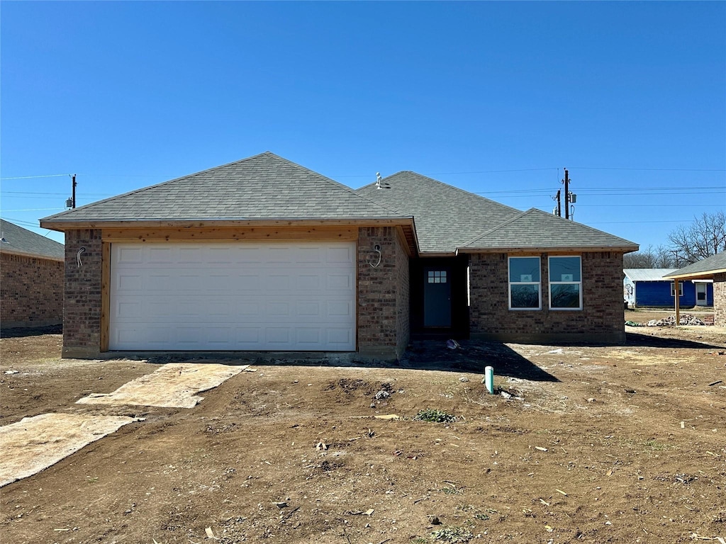 single story home with an attached garage, a shingled roof, and brick siding