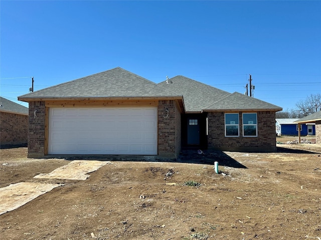 single story home with an attached garage, a shingled roof, and brick siding