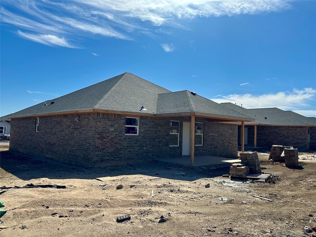 back of house featuring brick siding, a patio, and roof with shingles