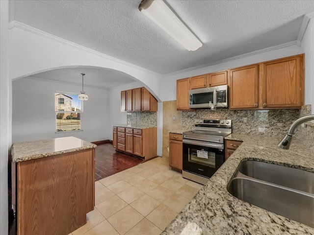 kitchen with pendant lighting, sink, light tile patterned floors, ornamental molding, and stainless steel appliances