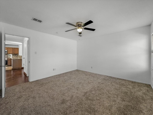 unfurnished room featuring ceiling fan, sink, and dark carpet