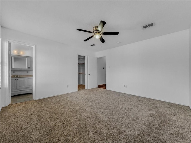 unfurnished bedroom featuring carpet floors, ensuite bath, ceiling fan, and a walk in closet