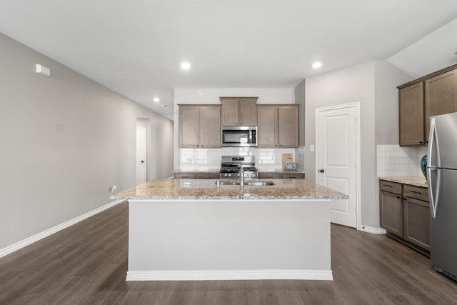 kitchen with a kitchen island with sink, decorative backsplash, light stone counters, and stainless steel appliances