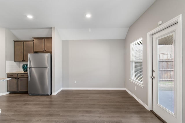 kitchen with dark wood-type flooring, vaulted ceiling, backsplash, and stainless steel refrigerator