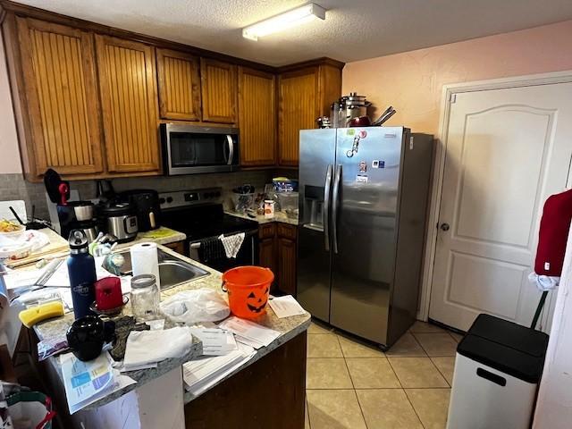 kitchen featuring a textured ceiling, appliances with stainless steel finishes, and light tile patterned flooring