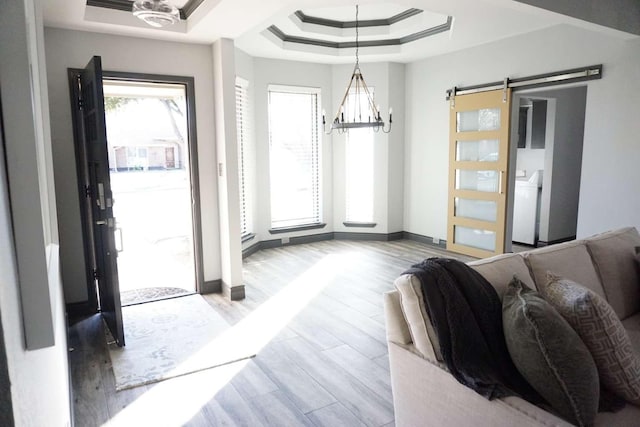 entrance foyer featuring a raised ceiling, a barn door, a chandelier, and light hardwood / wood-style floors