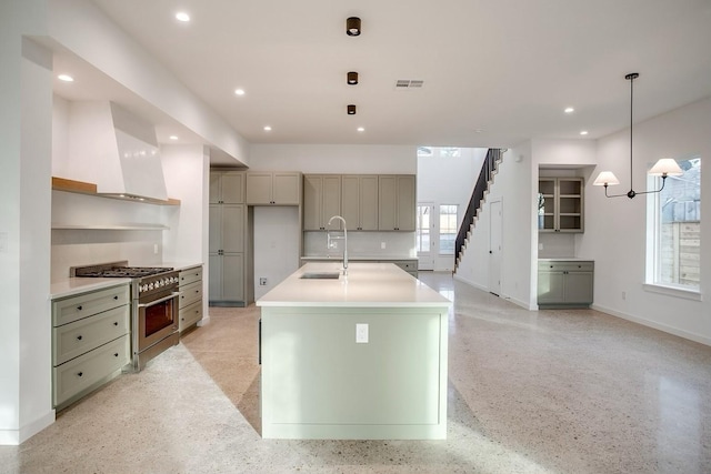 kitchen with premium range hood, decorative light fixtures, an island with sink, sink, and stainless steel range