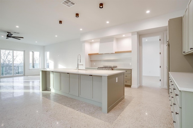 kitchen with a large island, wall chimney range hood, sink, gray cabinets, and ceiling fan